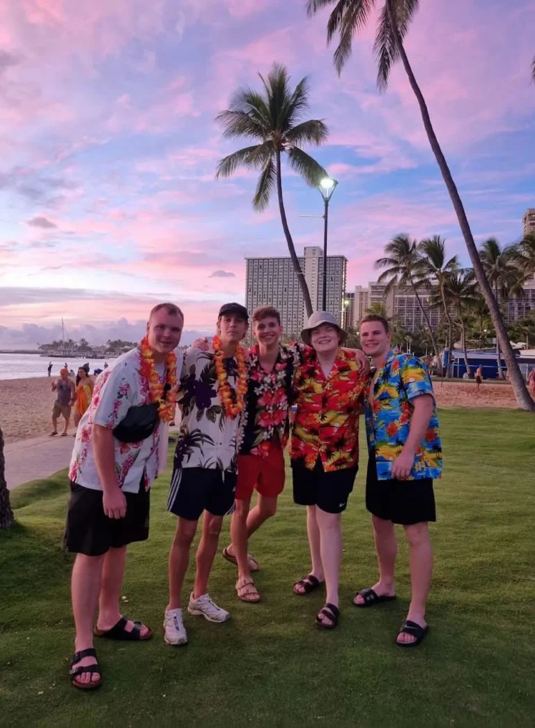 Fem højskoleelever står på stranden i Hawaiiskjorter til en smuk lille solnedgang på Hawaii på højskole i udlandet