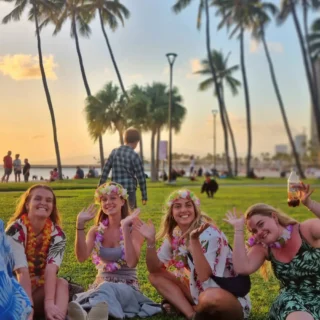fire højskoleelever vinger til kameraet, mens de sidder i hawaiiskjorter i en park på Hawaii på højskole i udlandet