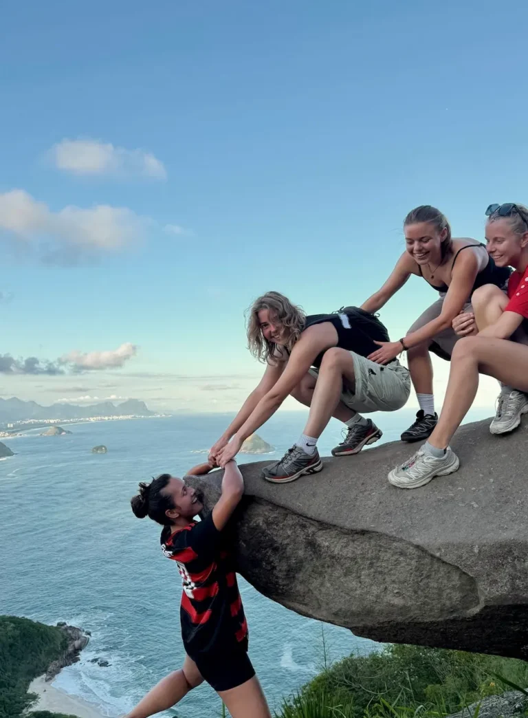 Elev hænger udover klippe i rio med to venner der smiler på højskole i udlandet