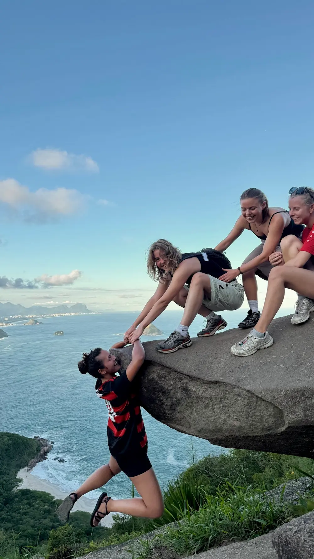 Elev hænger udover klippe i rio med to venner der smiler på højskole i udlandet