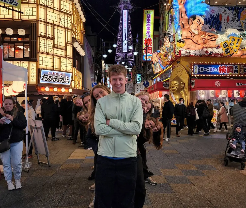 En højskoleelev står i midten af gaden i Osaka med neonlys bag ham på højskole i udlandet